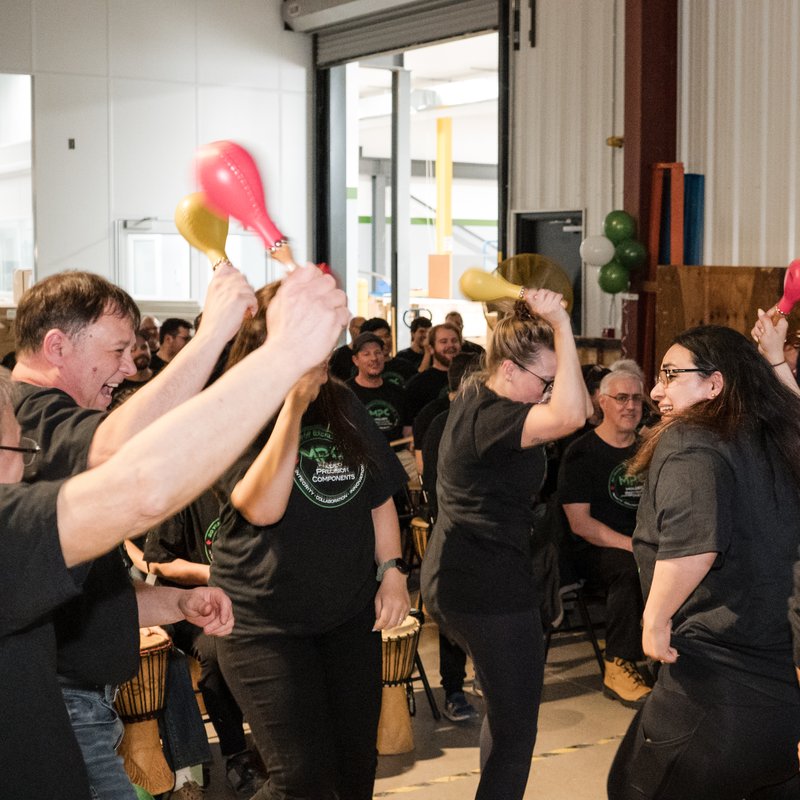 Colleagues laughing and dancing with shakers during a Drum Cafe team building session
